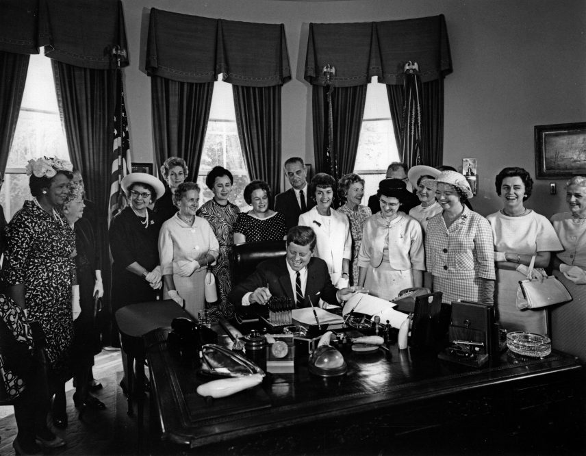 photo from 1964 of president John Kennedy signing the Equal Pay act. He is surrounded by Equal pay advocate, including AAUW members.