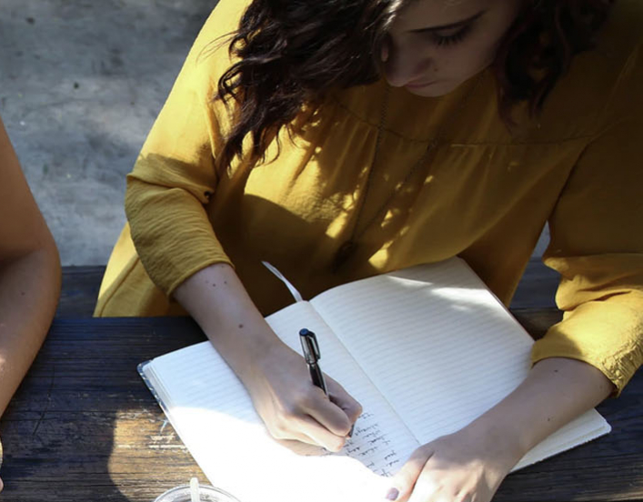 two women at an outdoor table reading and writing.