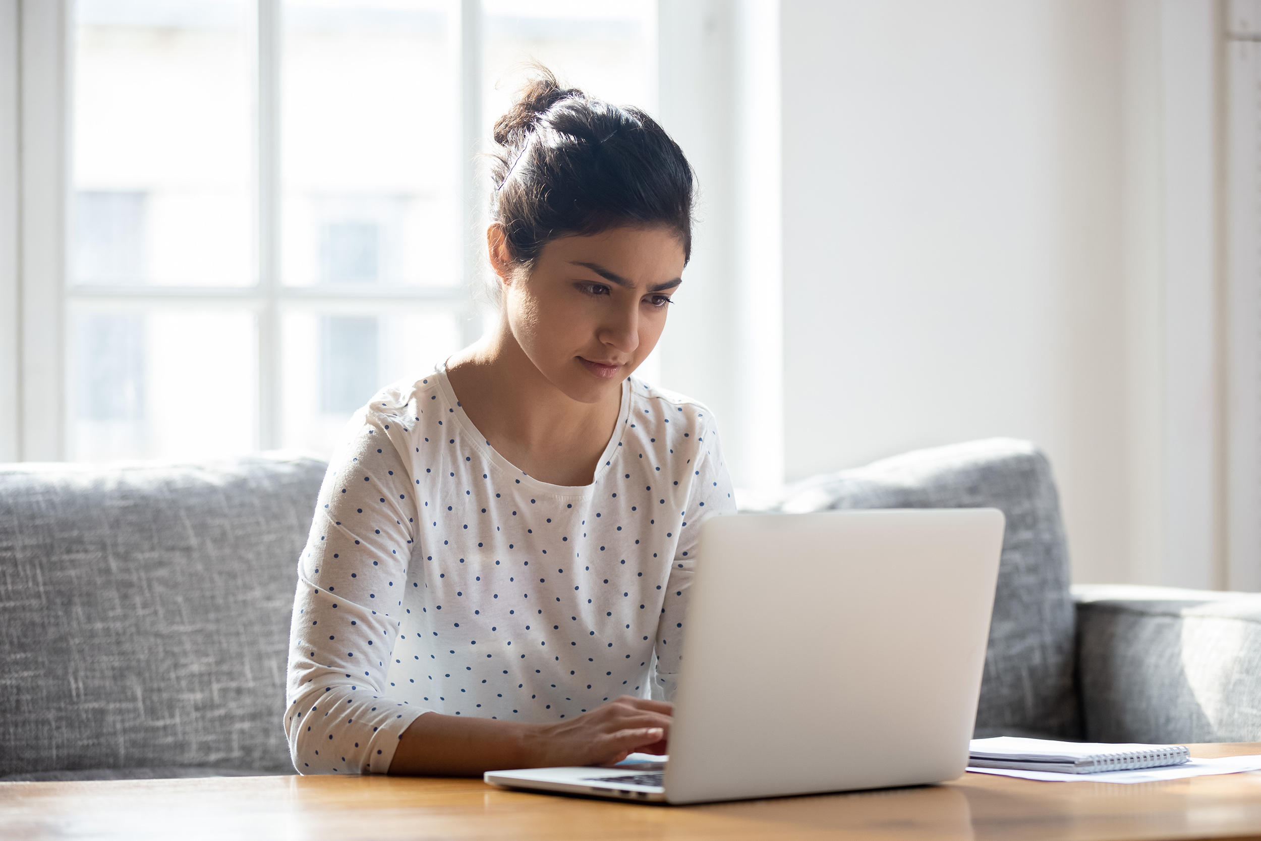 Focused young woman using laptop at home.