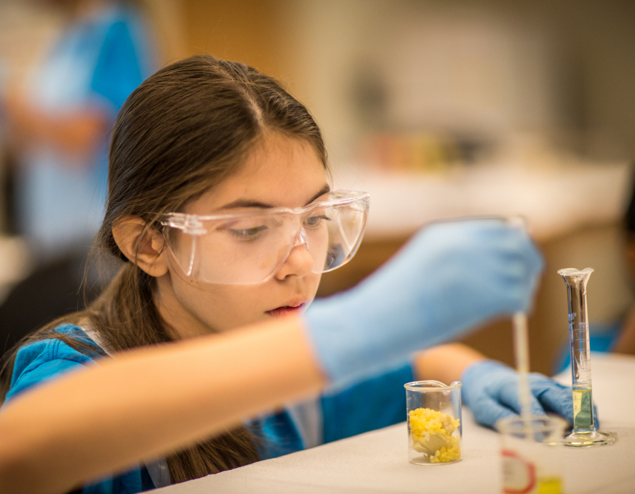 Young girl wearing safety goggles and gloves conducts chemical experiment in beaker.