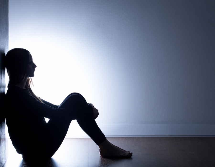 Sad-looking teenage girl sitting on floor alone in dark room