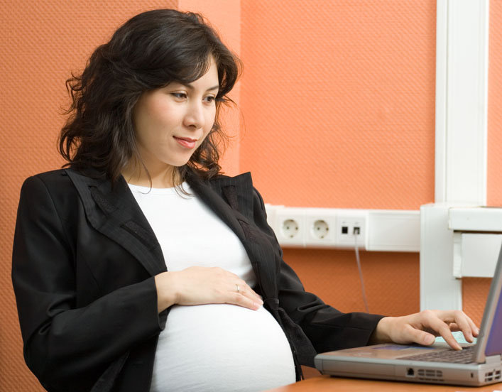 Pregnant woman, with hand on belly, in front of a laptop