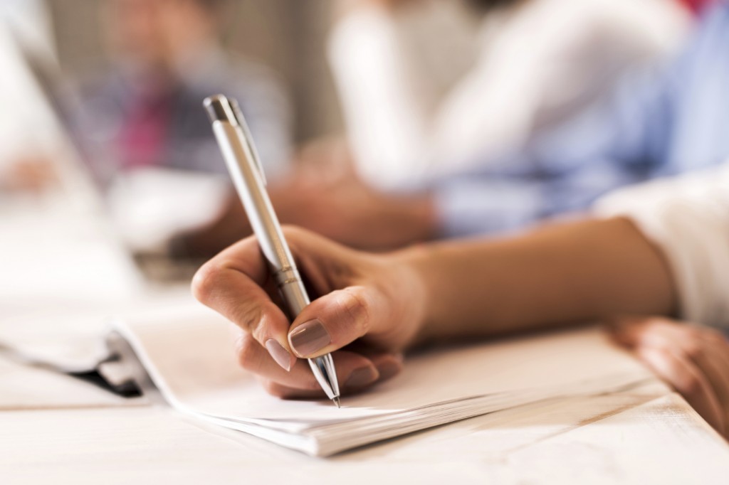 Close up of unrecognizable woman writing on a paper with a pen.