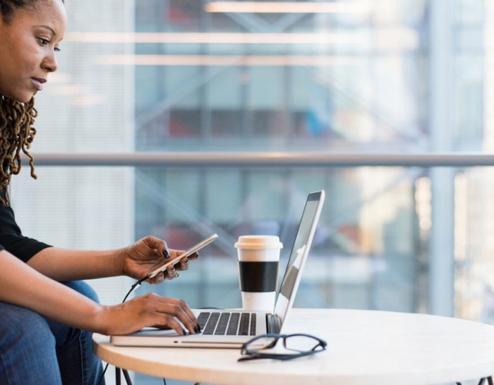 African American women at desk coding on her laptop and using a mobile phone