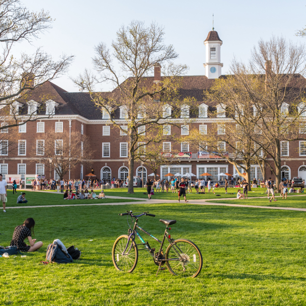 College students study and socialize on grassy area in front of campus building.