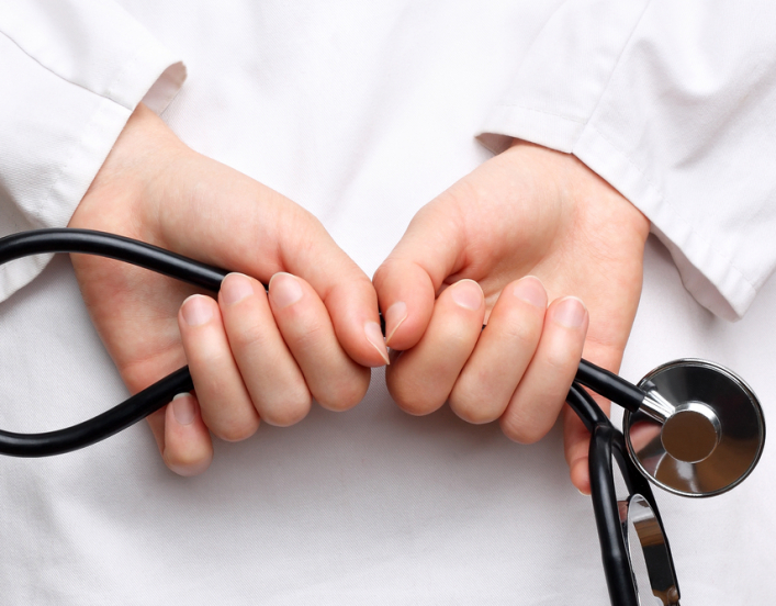 A doctor's hands holding a stethoscope behind her back.