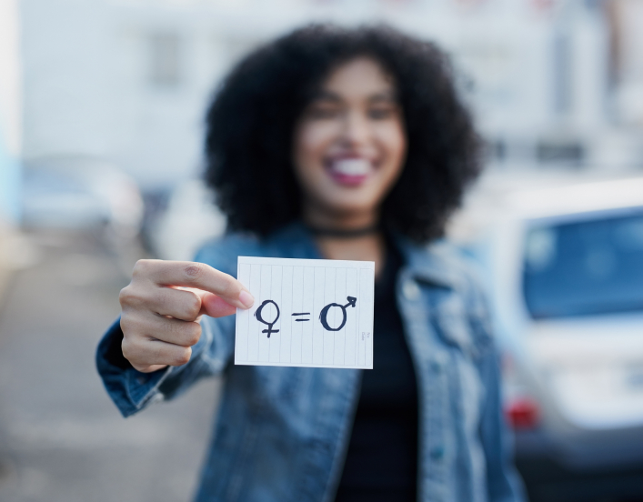 Out of focus woman holding a piece of paper with gender symbols and equals sign drawn on it.