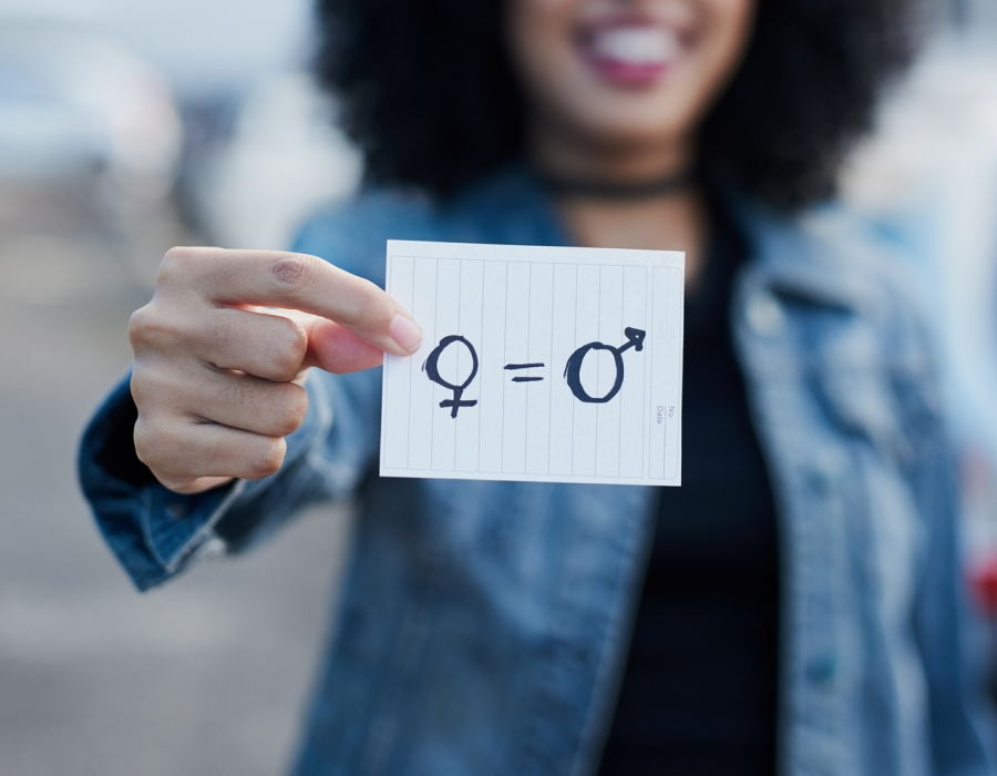 Out of focus woman holding a piece of paper with gender symbols and equals sign drawn on it.