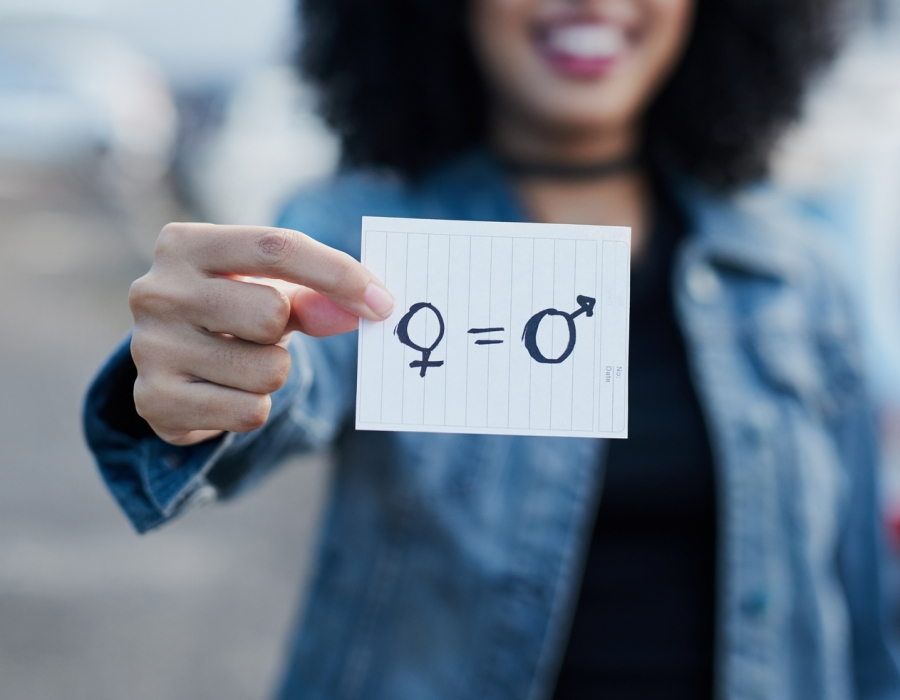 Out of focus woman holding a piece of paper with gender symbols and equals sign drawn on it.