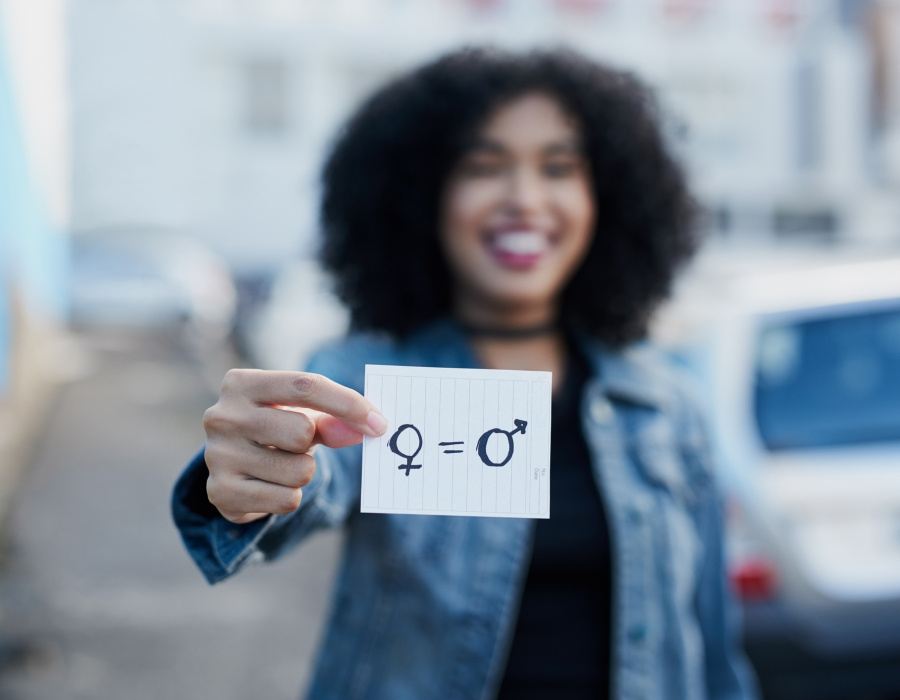 Out of focus woman holding a piece of paper with gender symbols and equals sign drawn on it.