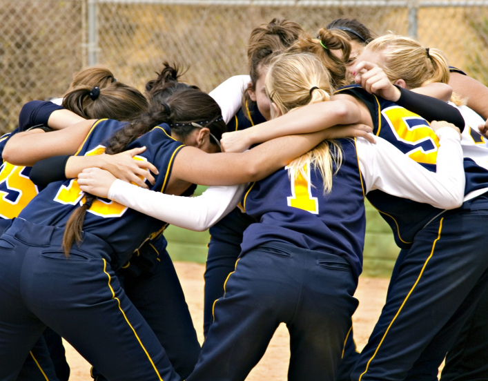 Group of girls in sports jerseys huddle before game.