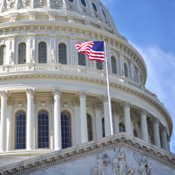 The dome of Capitol Building, Washington DC, and the American flag against a blue sky.