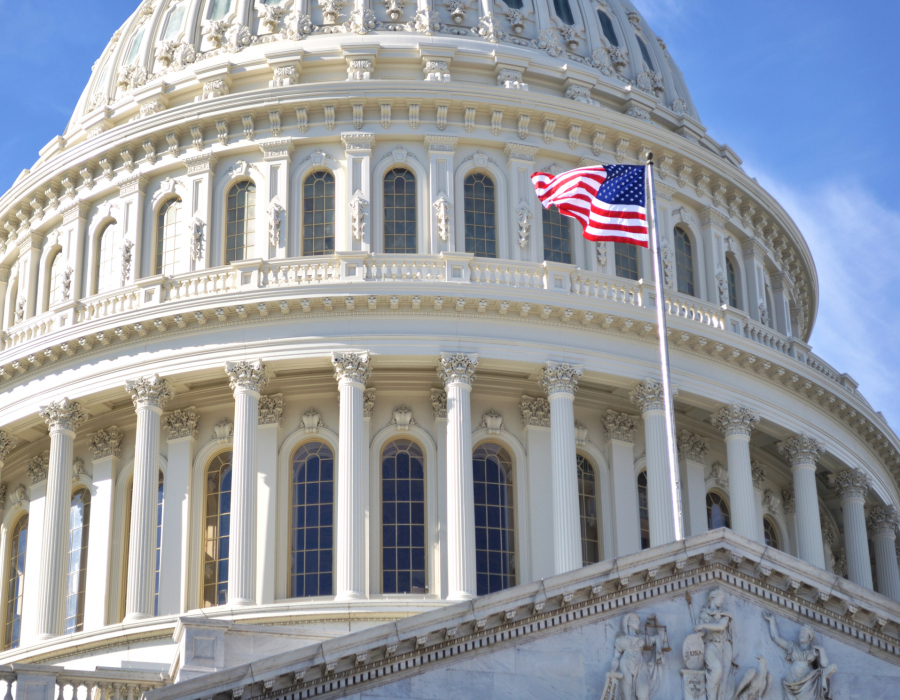 The dome of Capitol Building, Washington DC, and the American flag against a blue sky.