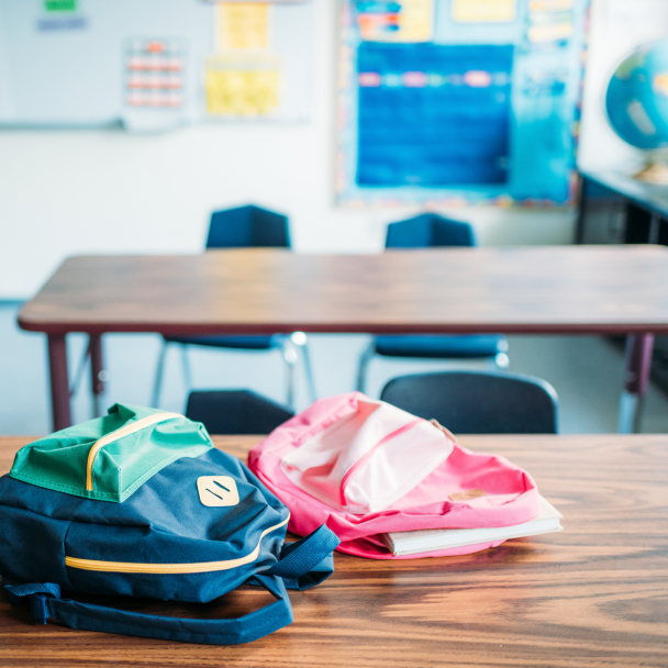 Two backpacks laying on desk in school classroom.