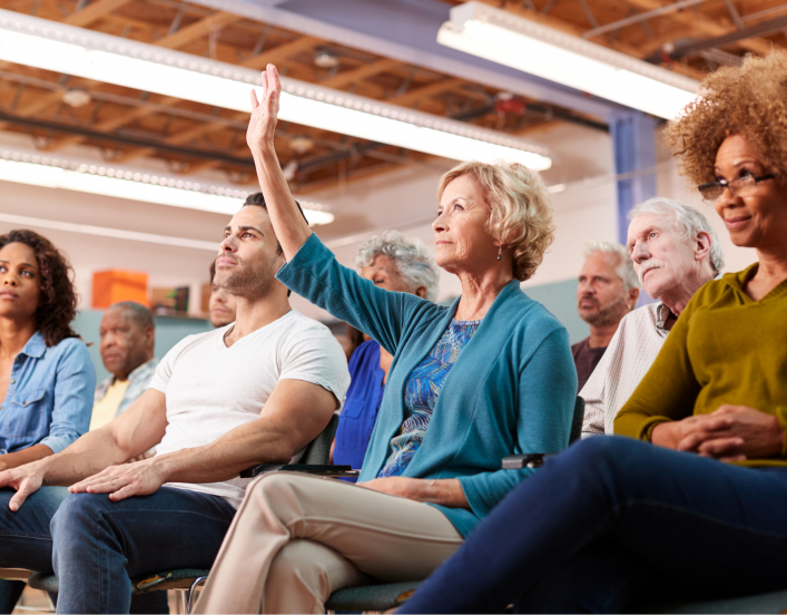 Photo of audience members at a town hall meeting. Woman raises hand.