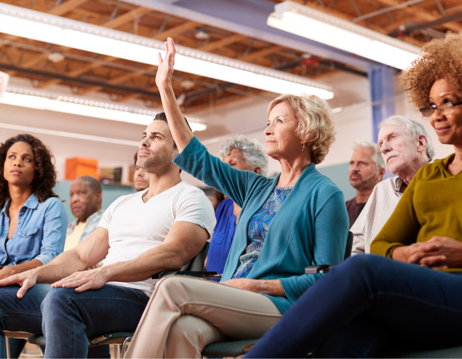 Photo of audience members at a town hall meeting. Woman raises hand.