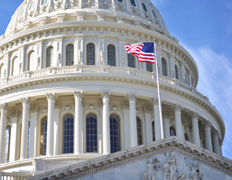 The dome of Capitol Building, Washington DC, and the American flag against a blue sky.