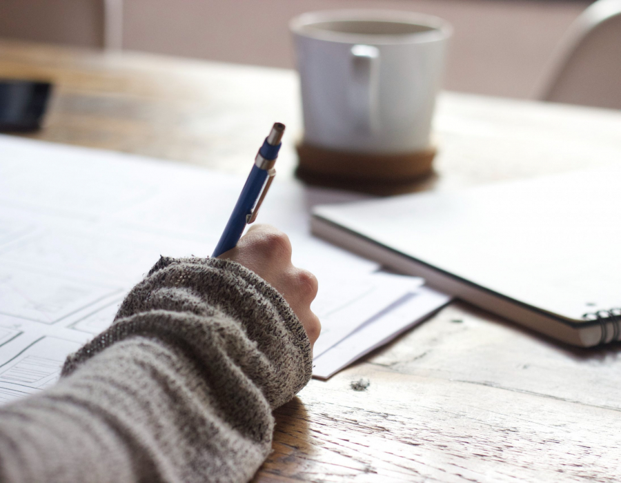 person writing with a pen at a table