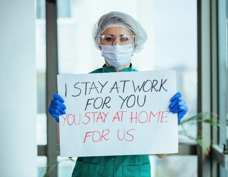 Female doctor holding placard with 'I stay at work for you, you stay at home for us' message during coronavirus pandemic.