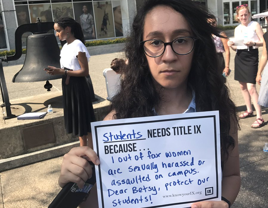 Student holding sign urging Title IX protections against harassment in front of US. Department of Education