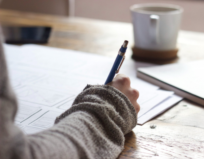 person writing with a pen at a table