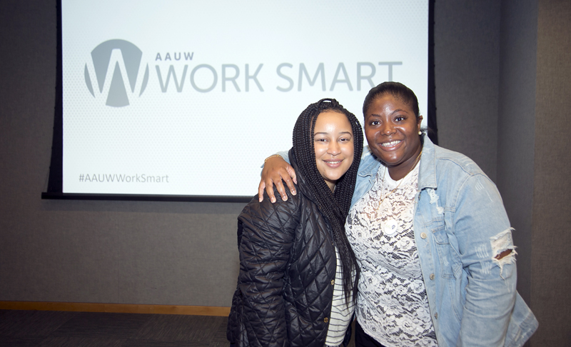 Two young Black women pose smiling with arms around each other in front of an AAUW Work Smart sign.