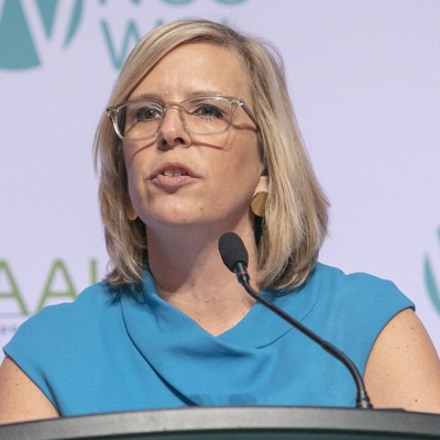 AAUW CEO Kim Churches speaking at a podium wearing a light blue dress