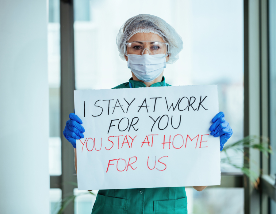 Female doctor holding placard with 'I stay at work for you, you stay at home for us' message during coronavirus pandemic.