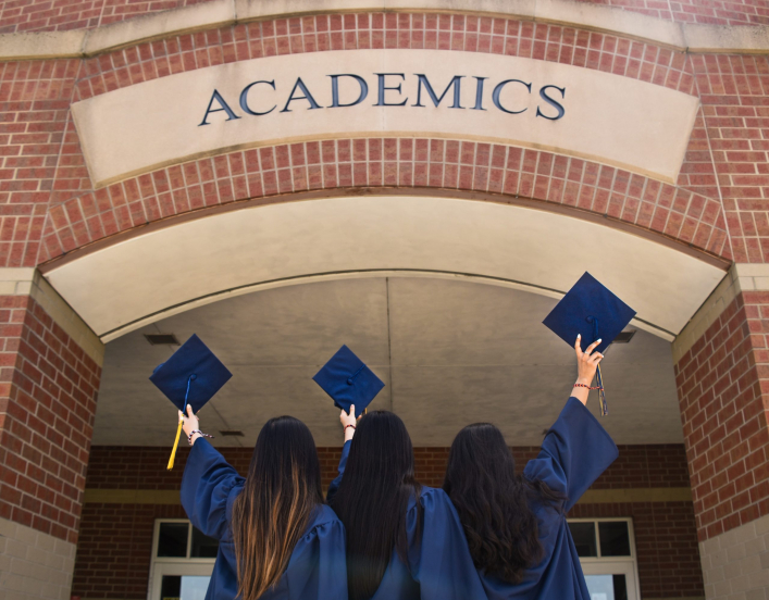 Three women with graduation gowns holding their caps in the air