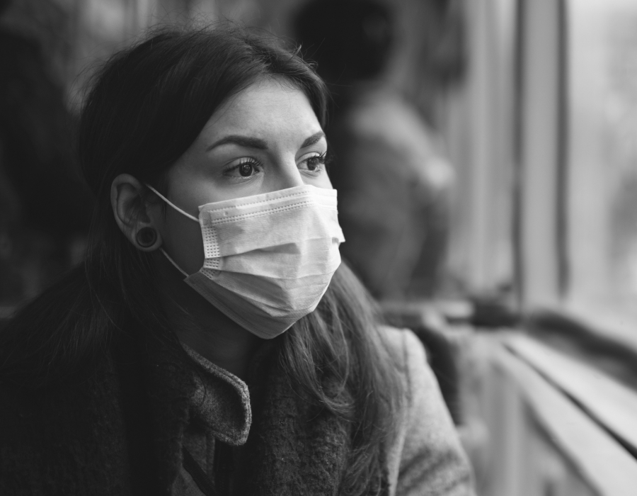 Black and white photo of a latina woman looking out a window wearing a surgical mask.