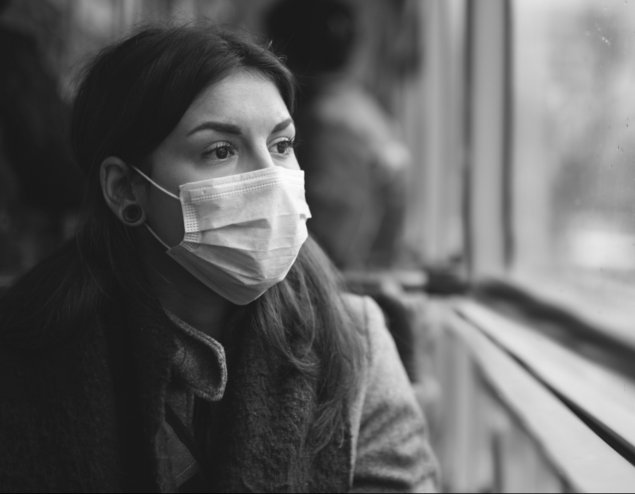 Black and white photo of a latina woman looking out a window wearing a surgical mask.