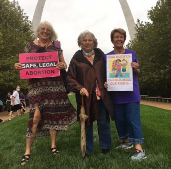 Photo of AAUW members standing in front of the Gateway Arch in St. Louis, MO holding signs.