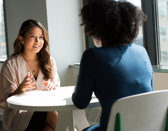 Two professional women talking across a table from one another.