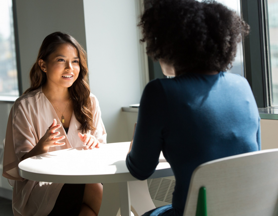 Two professional women talking across a table from one another.