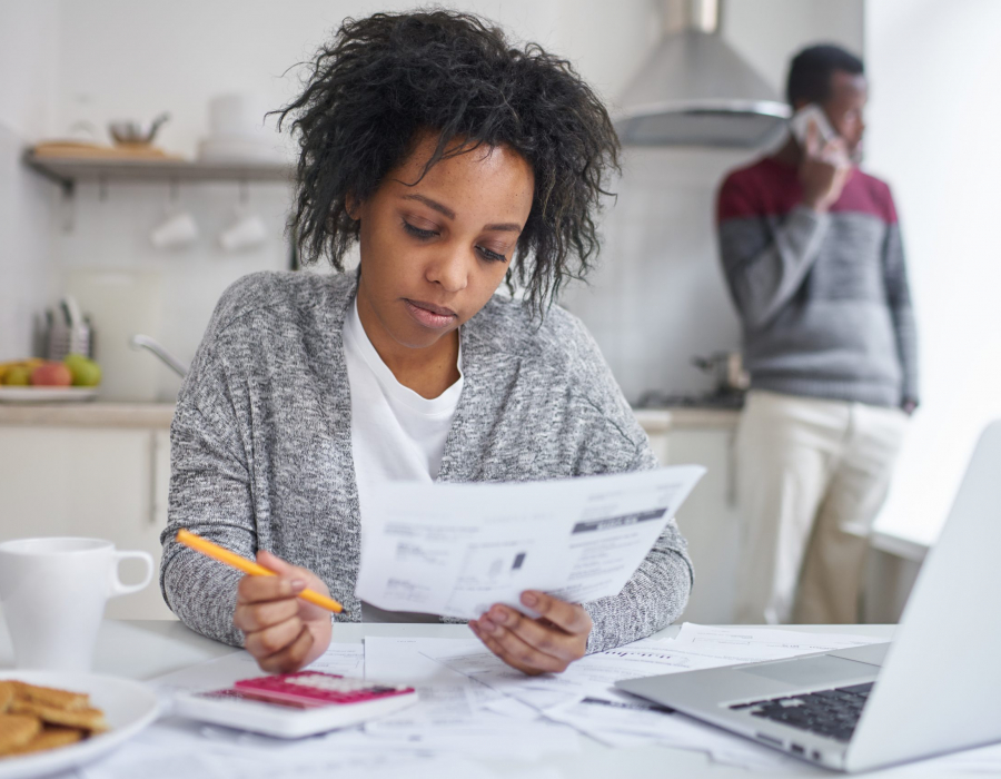 Photo of young Black woman sitting at the kitchen table paying bills online.