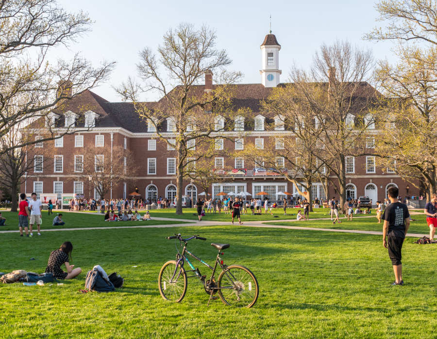 College students study and socialize on grassy area in front of campus building.