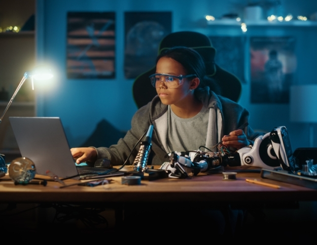 Young Teenage Multiethnic Schoolgirl is Studying Electronics and Soldering Wires and Circuit Boards in Her Science Hobby Robotics Project. Girl is Working on a Robot in Her Room. Education Concept.